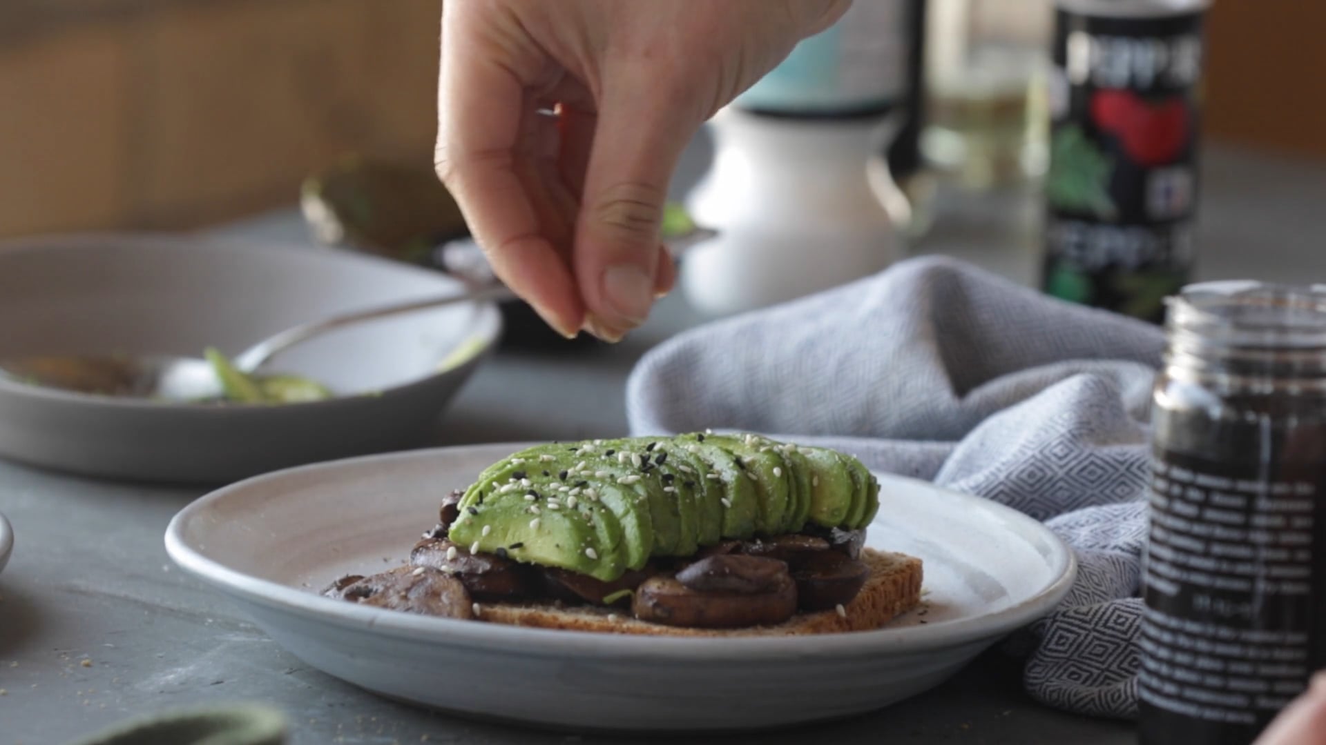 Hand sprinkling seeds on top of avocado toast