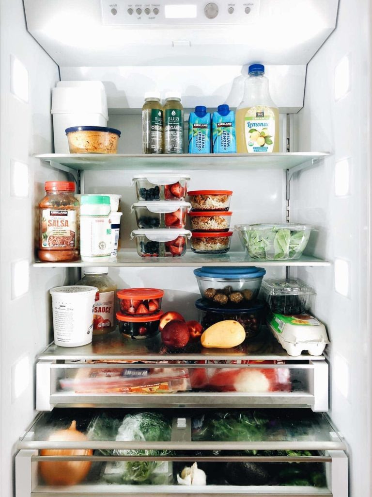 A photograph the inside of a refrigerator filled with juice, glass containers, eggs, salsa, and vegetables.