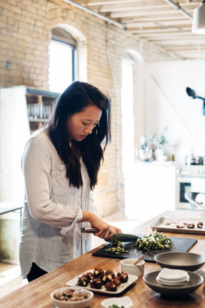 Woman chopping up vegetables on a black cutting board in a kitchen